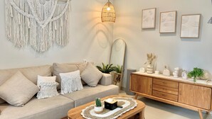 Uma sala de estar moderna com um sofá bege, decoração de macramé na parede, um armário de madeira e um espelho.