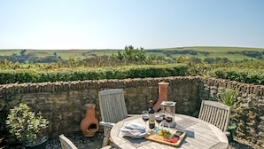 An outdoor dining area with a table set for two, surrounded by stone walls and potted plants. - Strand Cottage - Burton Bradstock, Bridport (Burton Bradstock)