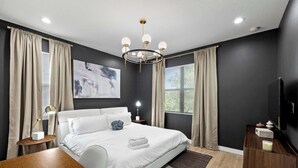 A modern bedroom with a large bed, a chandelier, and a flat-screen TV.