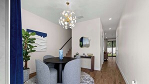 A modern dining area with a round table, grey upholstered chairs, a blue vase, and a decorative chandelier.