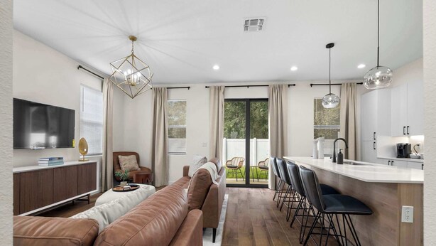 A modern living room with a brown leather sofa, a dining area with bar stools, and a kitchen with a white countertop.