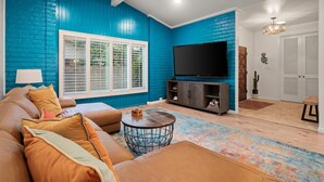 Ein Wohnzimmer mit blauer Akzentwand, einem großen Flachbildfernseher, einem braunen Ledersofa und einem runden Couchtisch.