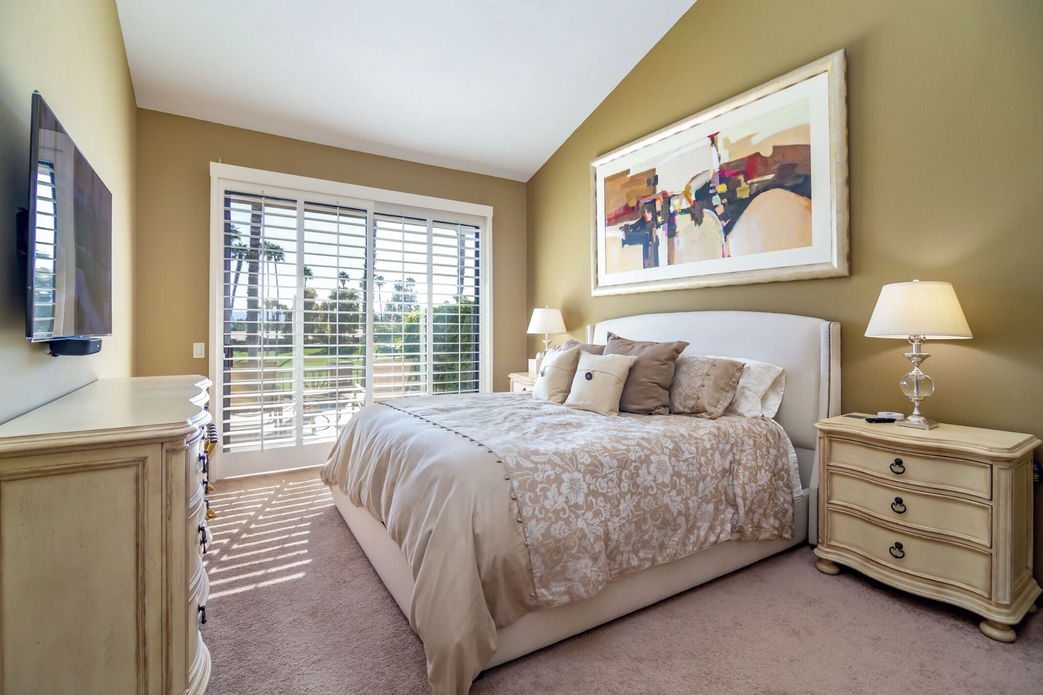 A bedroom with a large bed, a nightstand, a TV, and a window with blinds.