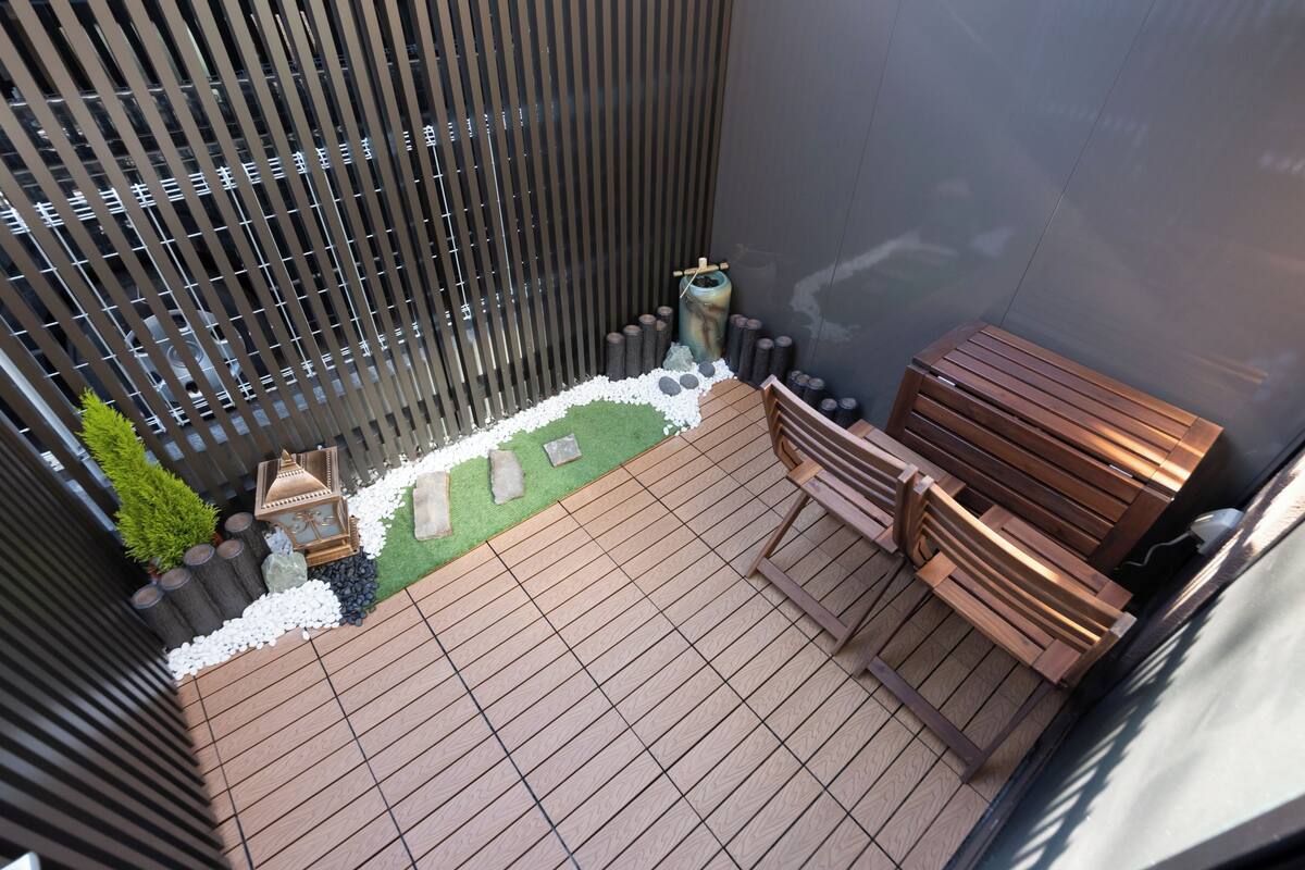 A rooftop terrace with a wooden deck, a small garden area with white pebbles and a green lawn, a wooden bench, and a lantern.