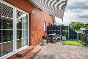 A brick house with a large sliding glass door, a patio with a table and chairs, and a grill. - Apartment 'Ferienwohnung An Der Haferkoppel' with Private Terrace and Wi-Fi (Groß Kussewitz)