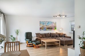A modern living room with a sectional sofa, a wooden coffee table, a green armchair, and a painting of a cityscape. - Apartment 'Ferienwohnung An Der Haferkoppel' with Private Terrace and Wi-Fi (Groß Kussewitz)