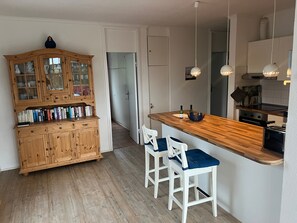 Eine Küche mit einem Holzkasten, zwei Barhocker, einer Holzausziehtafel und Pendelleuchten.