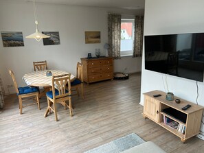 Ein Essbereich mit einem runden Tisch, Stühlen, einer Holzkommode, einem Fernseher und einem Bücherregal.