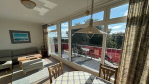 A spacious room with a large sliding glass door leading to an outdoor deck, a round table with chairs, a sofa, and a ceiling fan.