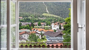 A view from a window overlooking a town with houses, a church, and a forested mountain. - Holiday Home 'Zaunkönig' with Mountain View and Private Terrace (Mittenwald)