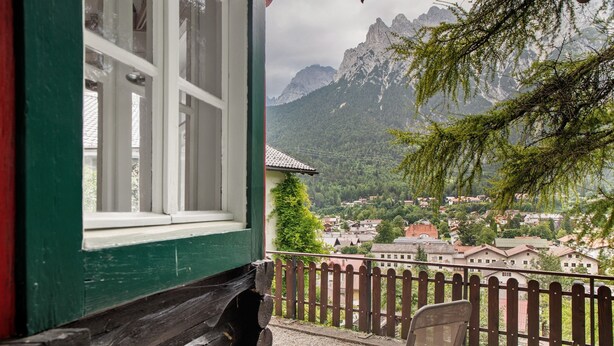 A balcony with a chair, a wooden fence, and a view of a village and mountains. - Holiday Home 'Zaunkönig' with Mountain View and Private Terrace (Mittenwald)