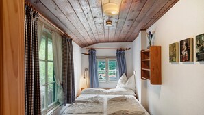 A bedroom with a wooden ceiling, a bed with white linens, a window with curtains, and a wooden nightstand. - Holiday Home 'Zaunkönig' with Mountain View and Private Terrace (Mittenwald)