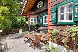 Una baita di legno con un patio steso in ghiaia, un tavolo di legno e due sedie.
