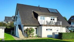 A two-story residential building with a sloped roof, solar panels, a small balcony, and a well-maintained lawn. - Apartment 'Ferienwohnung Baltic Sea' with Private Terrace, Private Garden and Wi-Fi (Börgerende-Rethwisch)