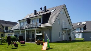 A two-story house with a balcony, a slide, and a lawn. - Apartment 'Ferienwohnung Baltic Sea' with Private Terrace, Private Garden and Wi-Fi (Börgerende-Rethwisch)
