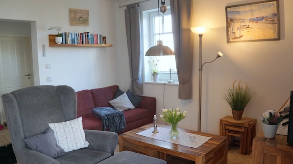 A living room with a grey armchair, a red sofa, a wooden coffee table, a floor lamp, and a painting on the wall.