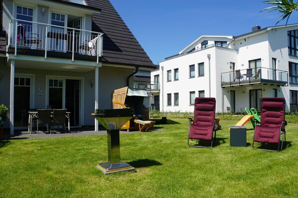 A residential building with a balcony, outdoor seating, and a grassy yard.