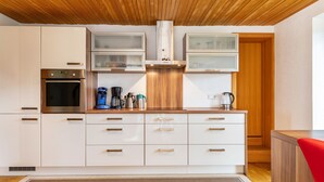 A modern kitchen with white cabinets, a stainless steel oven, a coffee maker, and a wooden ceiling.