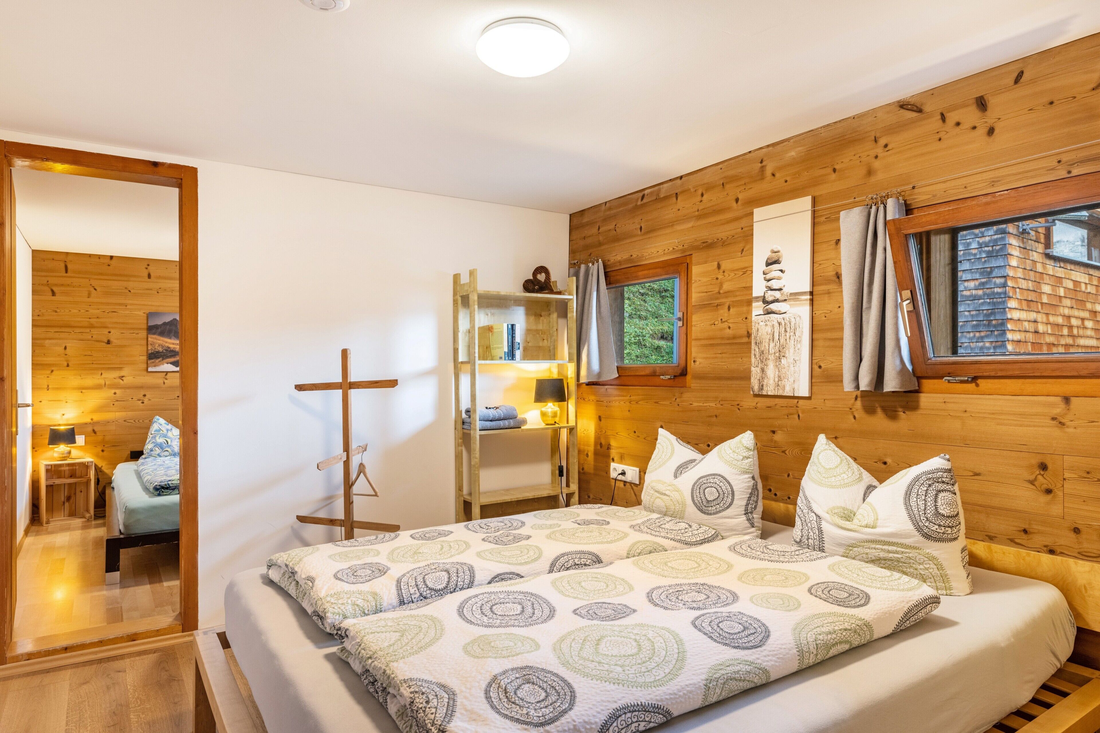 A wooden-paneled room with a bed, a wooden ladder, a shelf with books, and a window with curtains.