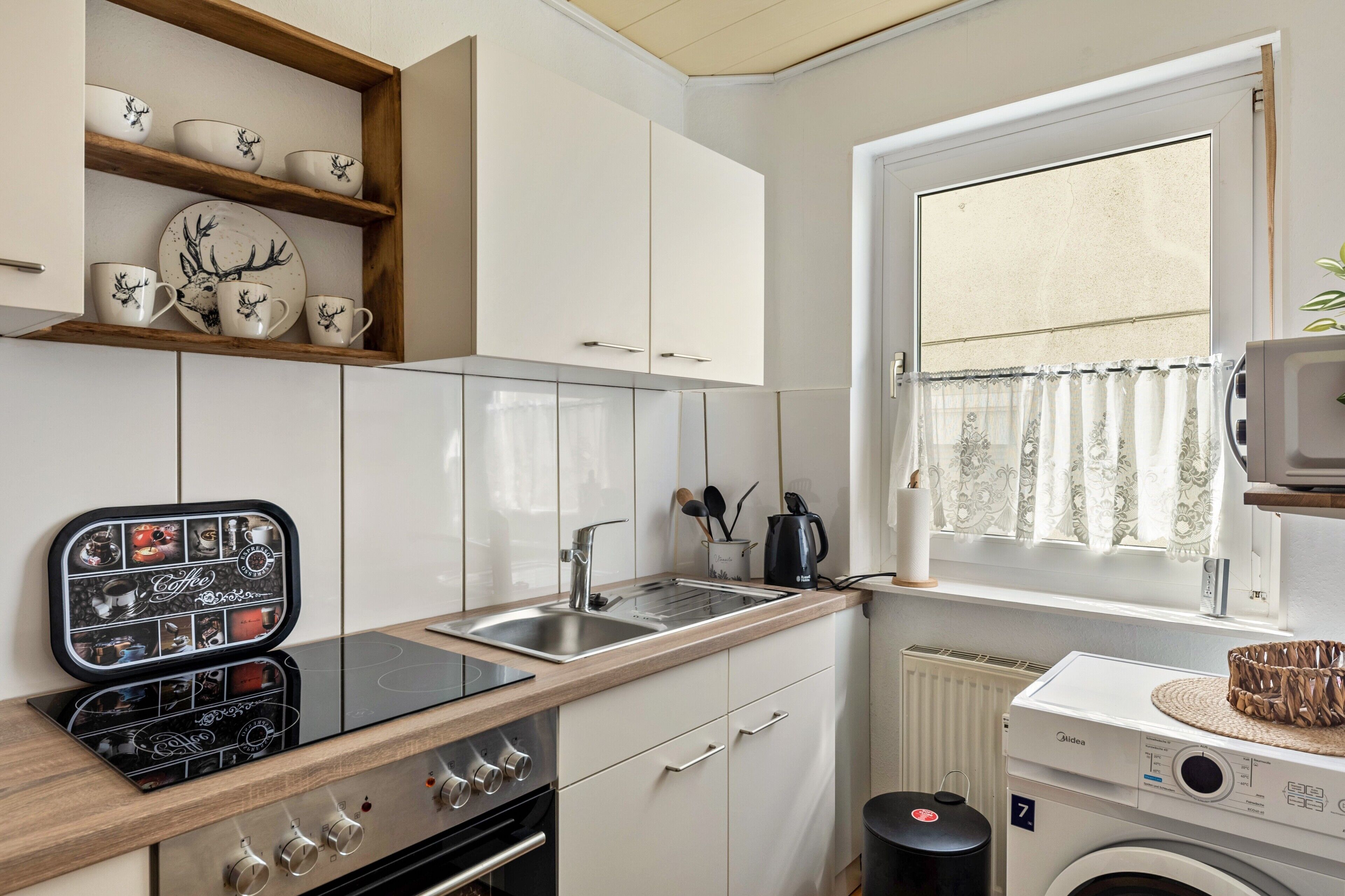 A compact kitchen with a built-in stove, a sink, and a window with curtains.