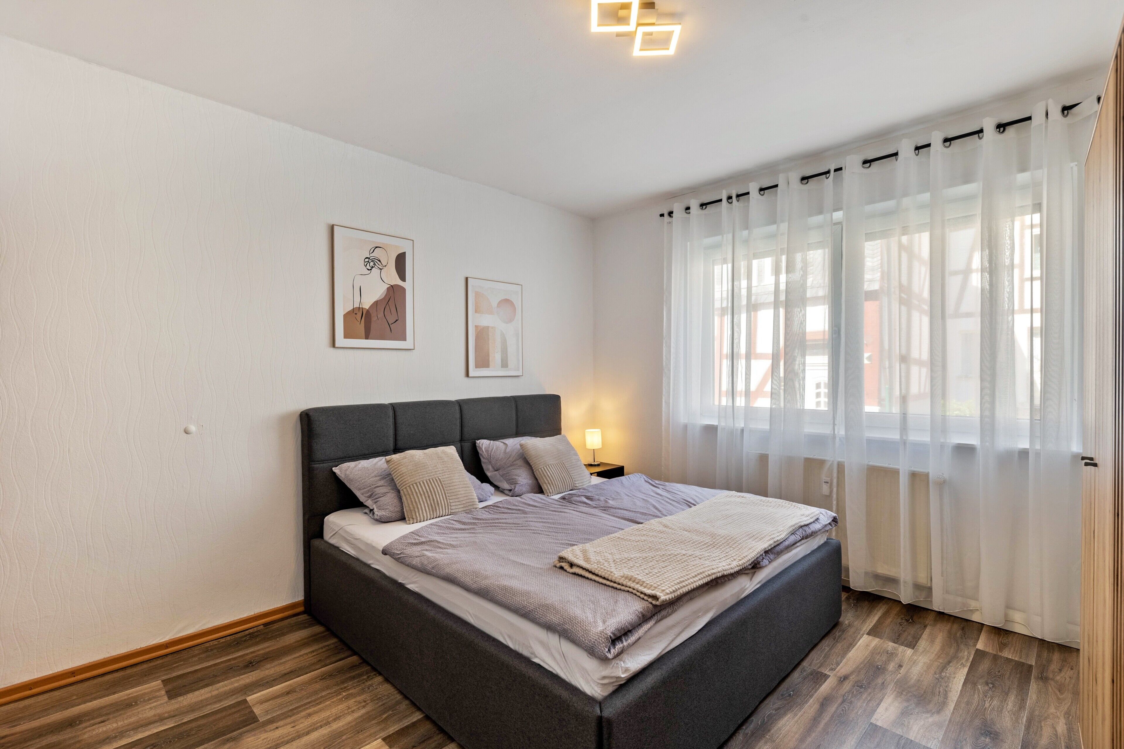 Een slaapkamer met een bed, gordijnen, een nachtkastje en wanddecoratie.