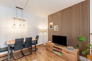 Un salon moderne comprenant une table à manger, des chaises, un téléviseur et un mur d’accent en bois.