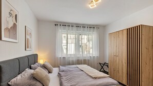 Une chambre à coucher comprenant un lit, une armoire, une fenêtre avec des rideaux légers et des œuvres d’art murales.