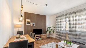Un salon moderne avec une table à manger en bois, un canapé, un téléviseur et une plante.