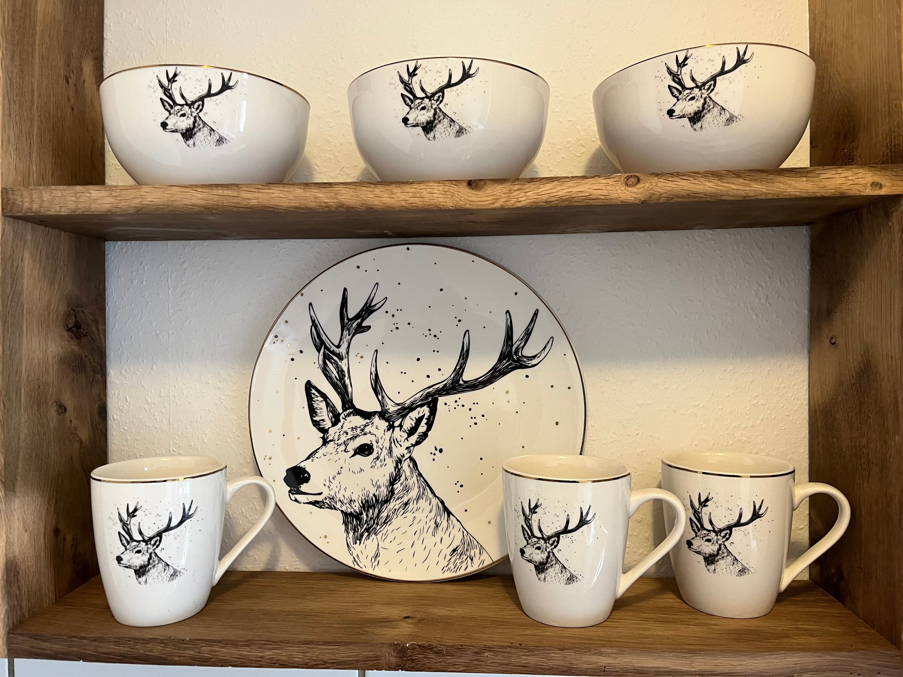 A set of white ceramic items with deer illustrations, including cups and a plate, displayed on wooden shelves.