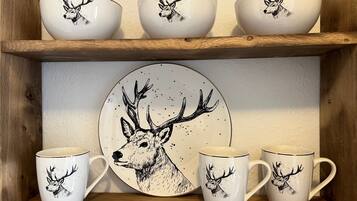 A set of white ceramic items with deer illustrations, including cups and a plate, displayed on wooden shelves.
