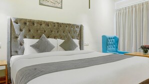A neatly made bed with a tufted headboard, two pillows, and a grey throw blanket. - Aangan Premium Shimla (Shimla)
