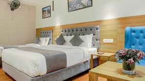 A hotel room with a large bed, a wooden headboard, a blue armchair, a small table with a vase of flowers, and two framed pictures on the wall. - Aangan Premium Shimla (Shimla)