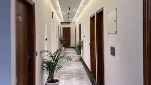 A hotel corridor with a marble floor, wooden doors, and potted plants. - The Crown Prince (Greater Noida)