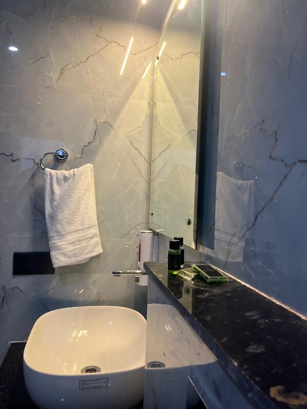 A bathroom with a white marble sink, a towel hanging on a rack, a mirror, and a black countertop.