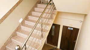 Uma escadaria com degraus de granito e corrimãos de metal que leva a uma porta de madeira com a inscrição 'ROOM NO. 101 TO 104'.