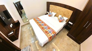 Quarto de hotel com uma cama grande, cabeceira de madeira, mesa de cabeceira com telefone e uma televisão em um suporte.
