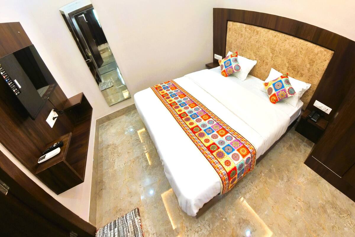 Une chambre d’hôtel avec un grand lit, une tête de lit en bois, une table de chevet avec un téléphone et un téléviseur posé sur un meuble.
