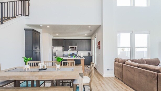 A spacious living area with a dining table and chairs, a sofa, and a kitchen in the background. - West Jordan Modern Home | Fenced Yard, New Build, Sleeps 7! (West Jordan)