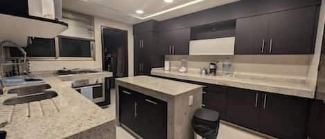 A modern kitchen with dark cabinetry, a central island, and a built-in oven.