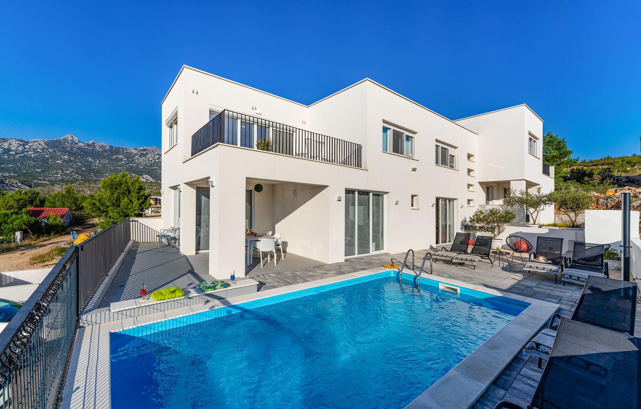 A modern two-story house with a swimming pool, outdoor seating, and a view of mountains.