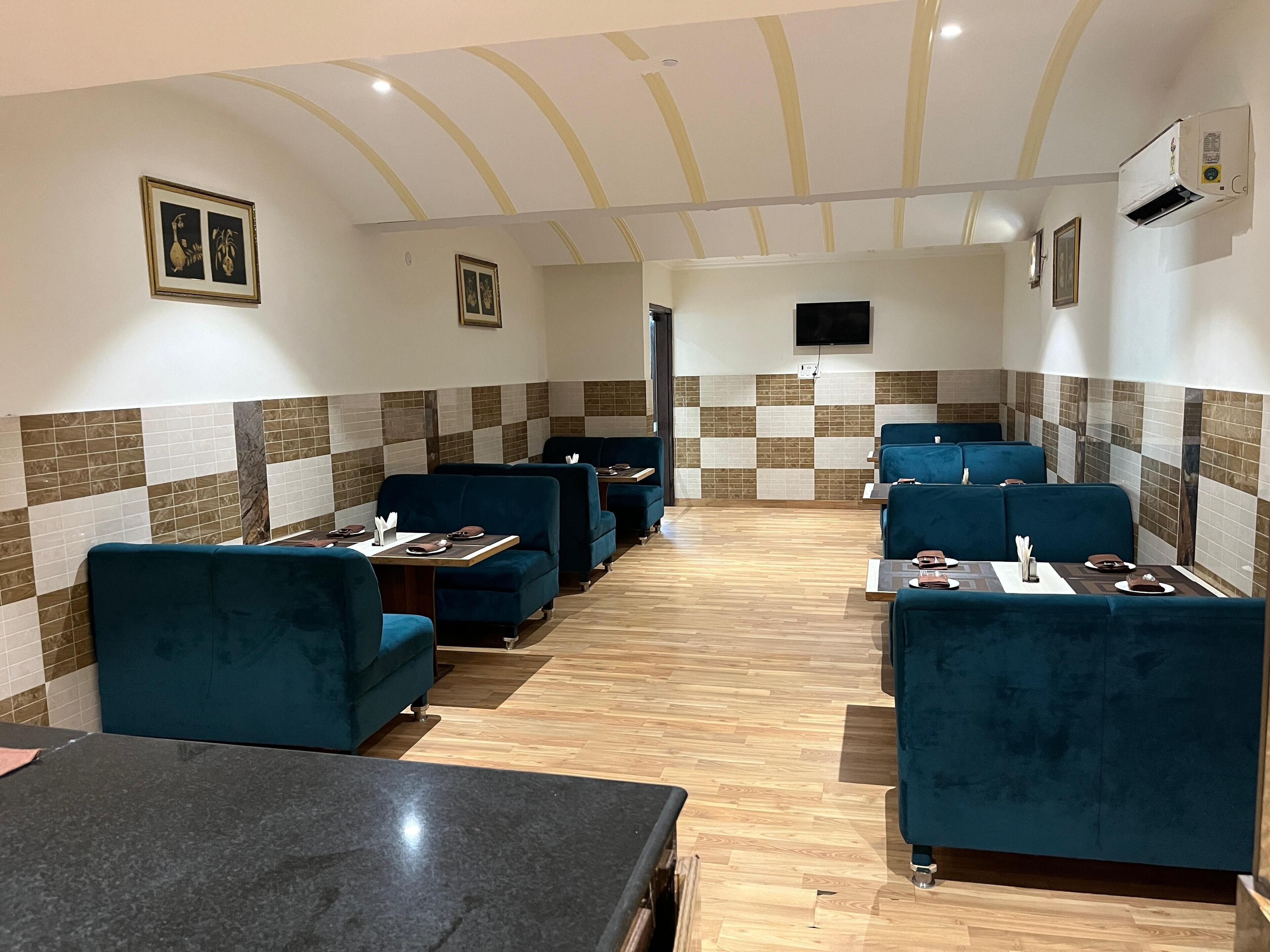 A restaurant with blue cushioned booths and black tables, featuring a checkered tile wall and a flat-screen TV mounted on the wall.