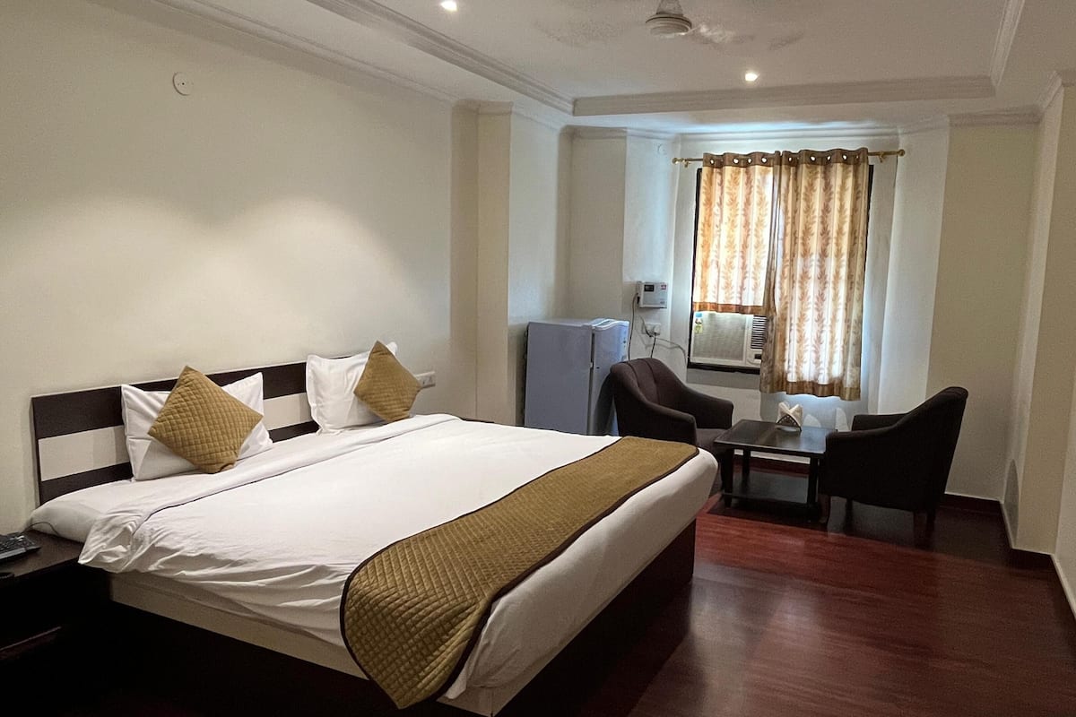 Una habitación de hotel con cama, escritorio, silla, televisor y aire acondicionado.