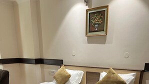 A neatly made bed with a quilted bedspread and pillows, a bedside table with a phone, and a wall-mounted picture frame. - Hotel Vasu International (Phagwara)