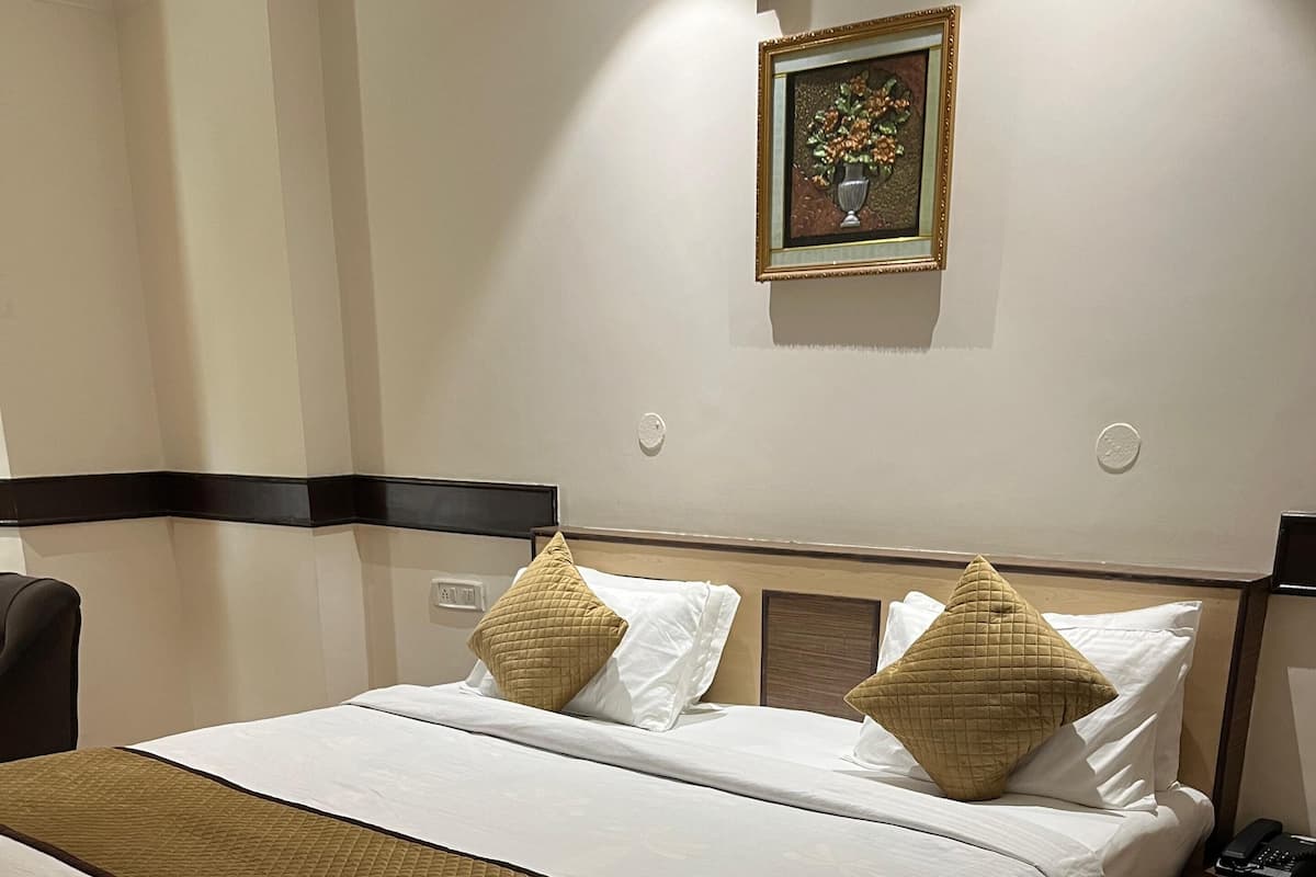 Una cama bien hecha con una colcha acolchada y almohadas, una mesita de noche con un teléfono, y un marco de fotos colgado en la pared.