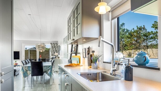 A modern kitchen with a large window, stainless steel appliances, and a dining area with a glass table. - "Isabel" - 600m from the sea by Interhome (Blokhus)