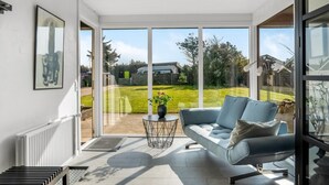 A modern living room with a grey sofa, a small round table, and a large glass door leading to a backyard. - "Isabel" - 600m from the sea by Interhome (Blokhus)