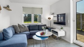 A modern living room with a sectional sofa, a coffee table, a flat-screen TV, and a large window offering a view of the outdoors. - "Isabel" - 600m from the sea by Interhome (Blokhus)
