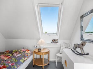 A bedroom with a bed, a small round table, a chair, a dresser, a mirror, and a window with a view of greenery.
