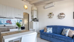 Una cocina moderna con armarios blancos, un sofá azul y una zona de comedor con sillas blancas.
