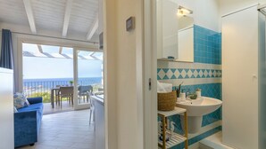Un baño moderno con lavabo, espejo y ducha. Tiene un balcón con mesa y sillas, y vistas al mar.